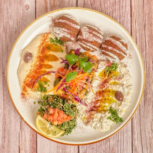 A Mediterranean platter with falafel, hummus, baba ghanoush, tabbouleh, and a lemon wedge.