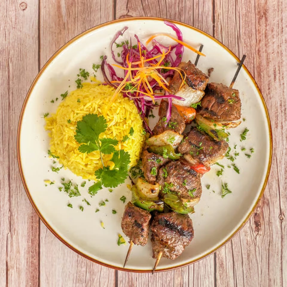 Two beef and vegetable skewers with yellow rice, garnished with cilantro and shredded cabbage.