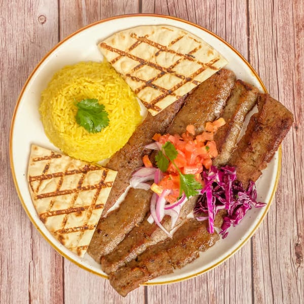 Mediterranean gyro plate with sliced meat, yellow rice, pita bread, diced tomatoes, onions, and red cabbage.