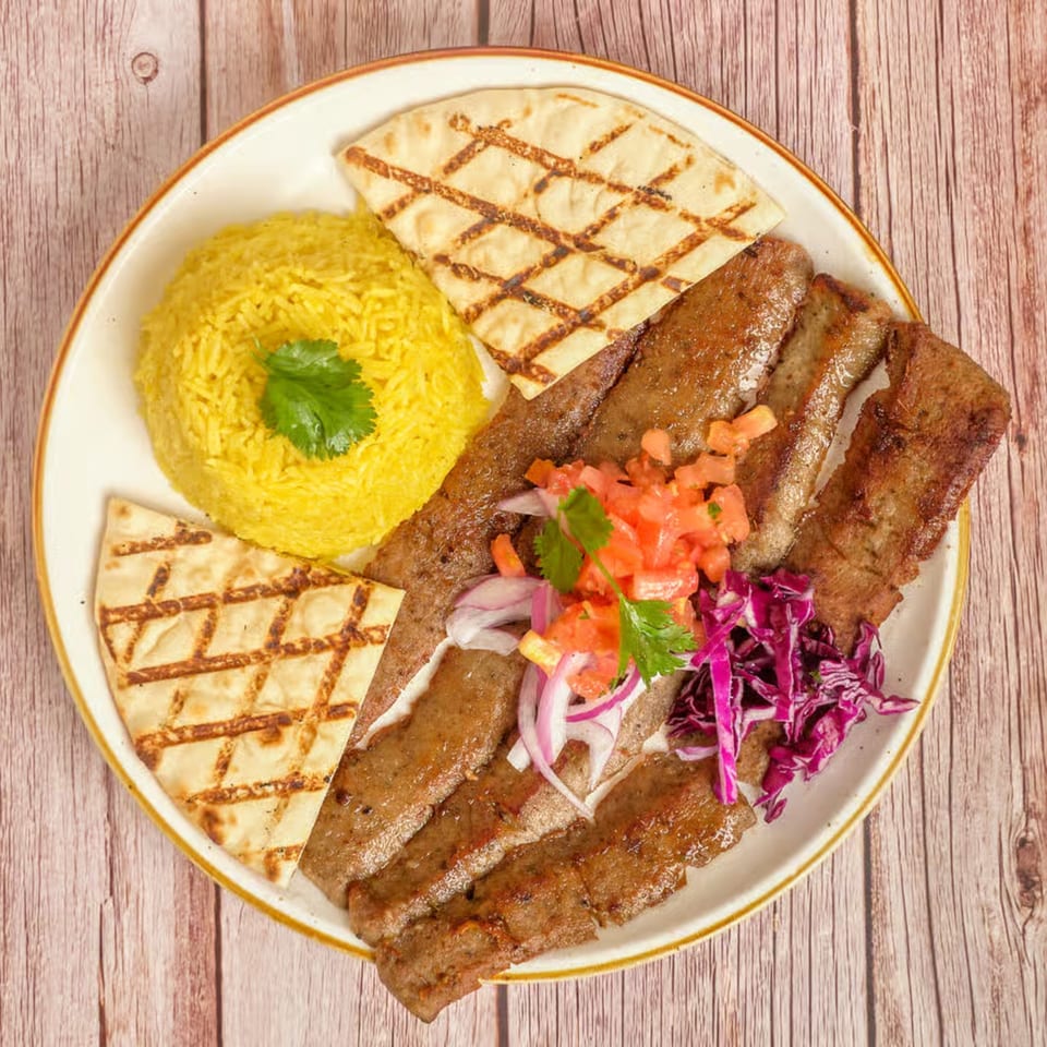 Mediterranean gyro plate with sliced meat, yellow rice, pita bread, diced tomatoes, onions, and red cabbage.