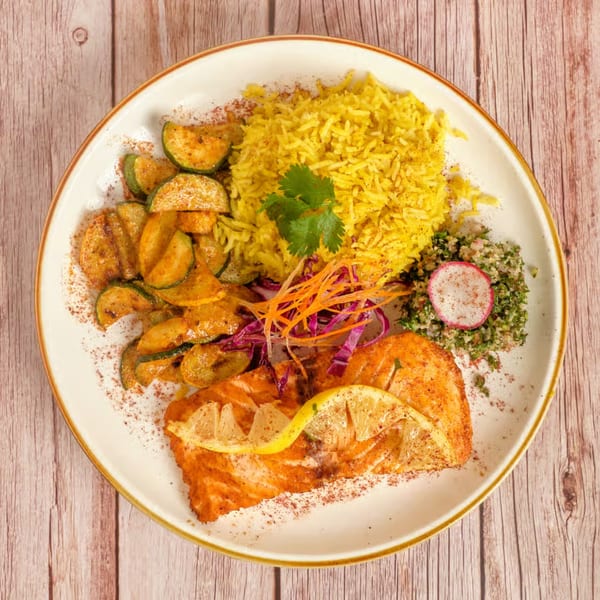 Mediterranean salmon dish with yellow rice, zucchini, tabbouleh, and lemon slices on a white plate.