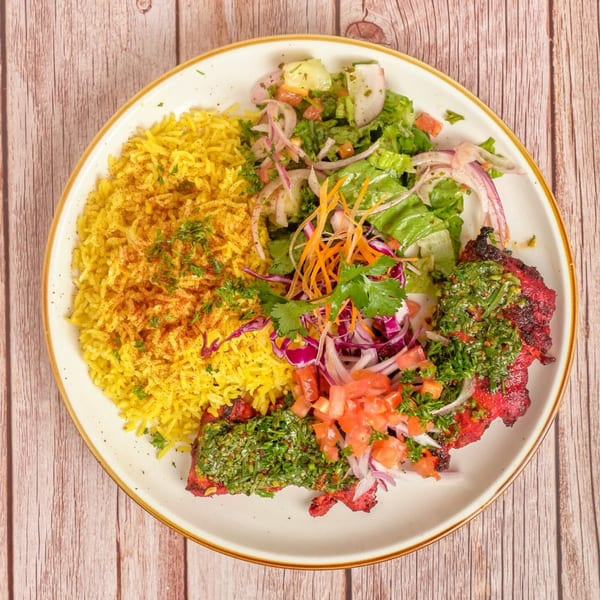 A Mediterranean dish with yellow rice, grilled red meat topped with green sauce, and a fresh salad.